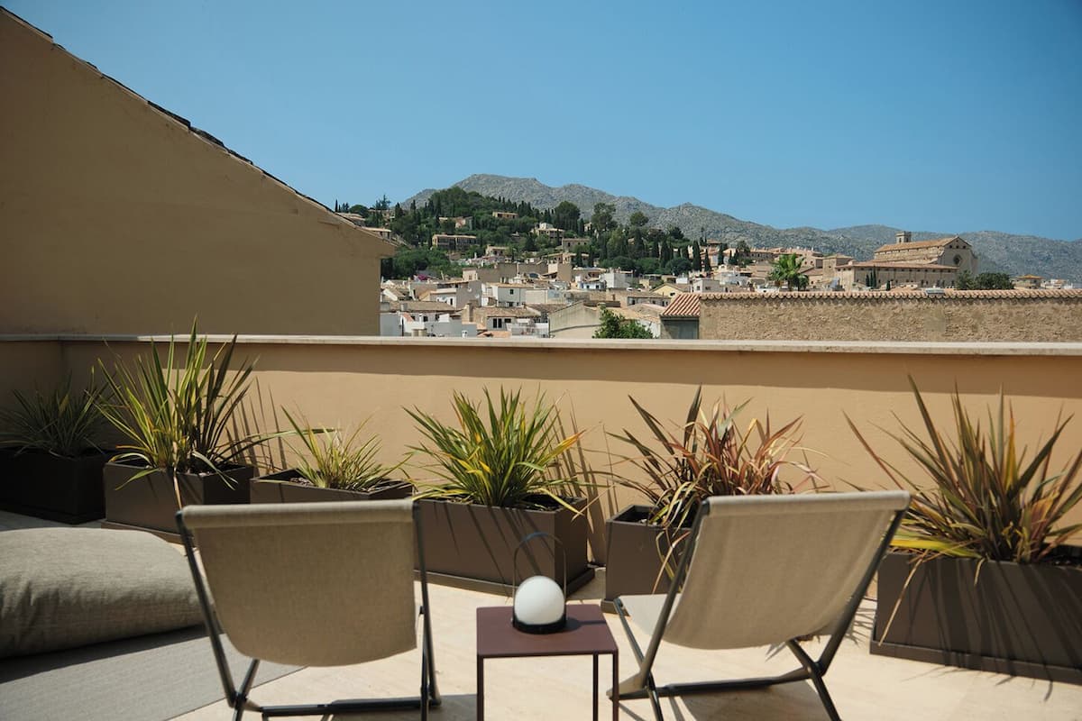 Une terrasse avec deux chaises et des plantes en pot, d’où l’on peut admirer une ville avec ses bâtiments et, au loin, des montagnes.
