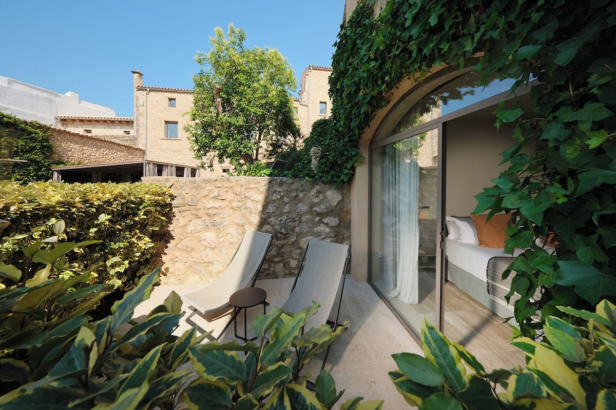 Un espace extérieur ensoleillé, aménagé avec deux fauteuils confortables et une petite table, entouré d’une végétation luxuriante et d’un mur de pierre.