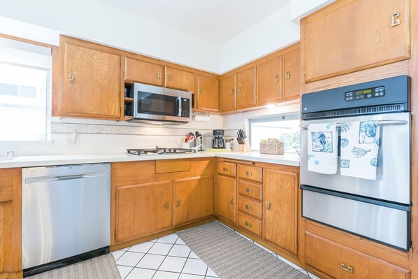 A kitchen with wooden cabinets, a microwave, a stove, a refrigerator, and a dishwasher. - Beautiful Bayfront Retreat with Unmatched Water Views (Newport Beach)