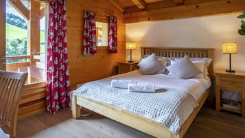 A wooden cabin bedroom with a bed, two bedside lamps, a wooden chair, and a window with curtains.