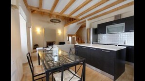 Een moderne keuken met zwarte kastjes, een glazen eettafel en houten balken in het plafond.