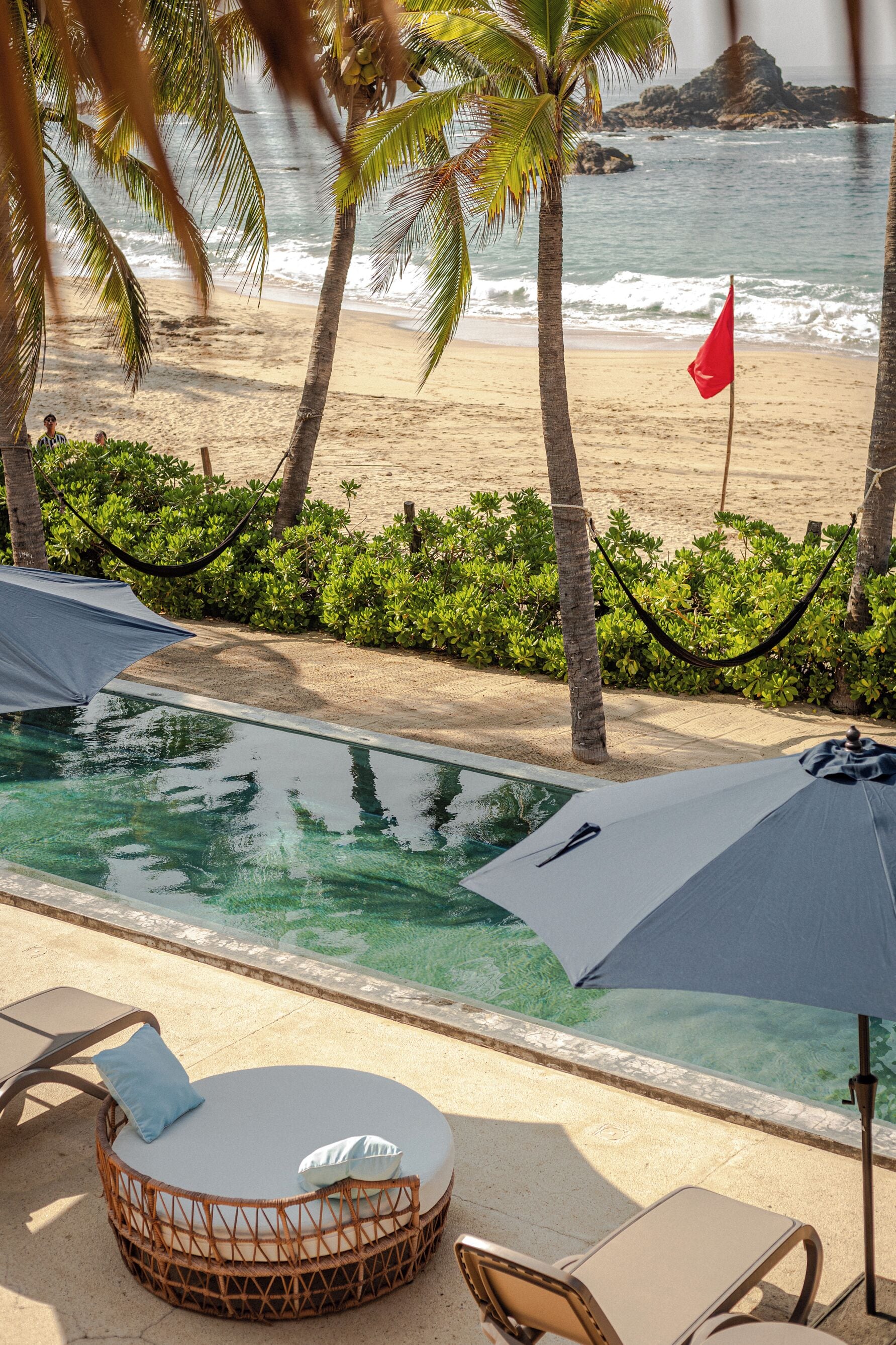 A poolside area with lounge chairs, a hammock, and a view of the beach and ocean.