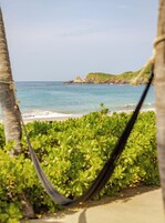 Una hamaca con vistas a una playa, con agua azul cristalina y una isla rocosa al fondo.