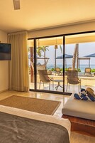 Habitación de hotel con un amplio ventanal corredero que da a un patio frente a la playa, con sillones reclinables y sombrillas.