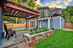 A backyard with a pergola, outdoor seating, a stone planter, and a pool.