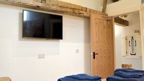 Une pièce avec un téléviseur à écran plat fixé au mur, une porte en bois et une pile de serviettes pliées posée sur le sol.