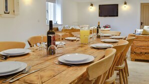 Un coin repas avec une table en bois mise pour le repas, entourée de chaises, et une bouteille de vin et une carafe de jus de fruits posées sur la table.