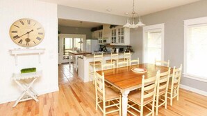 Un comedor con una mesa y sillas de madera, un reloj en la pared y una cocina al fondo.