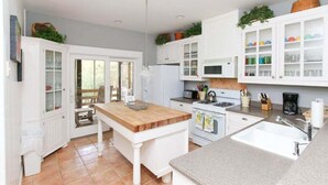 Una cocina con armarios blancos, una isla de madera, horno empotrado, un fregadero y ventana con vistas a un jardín.