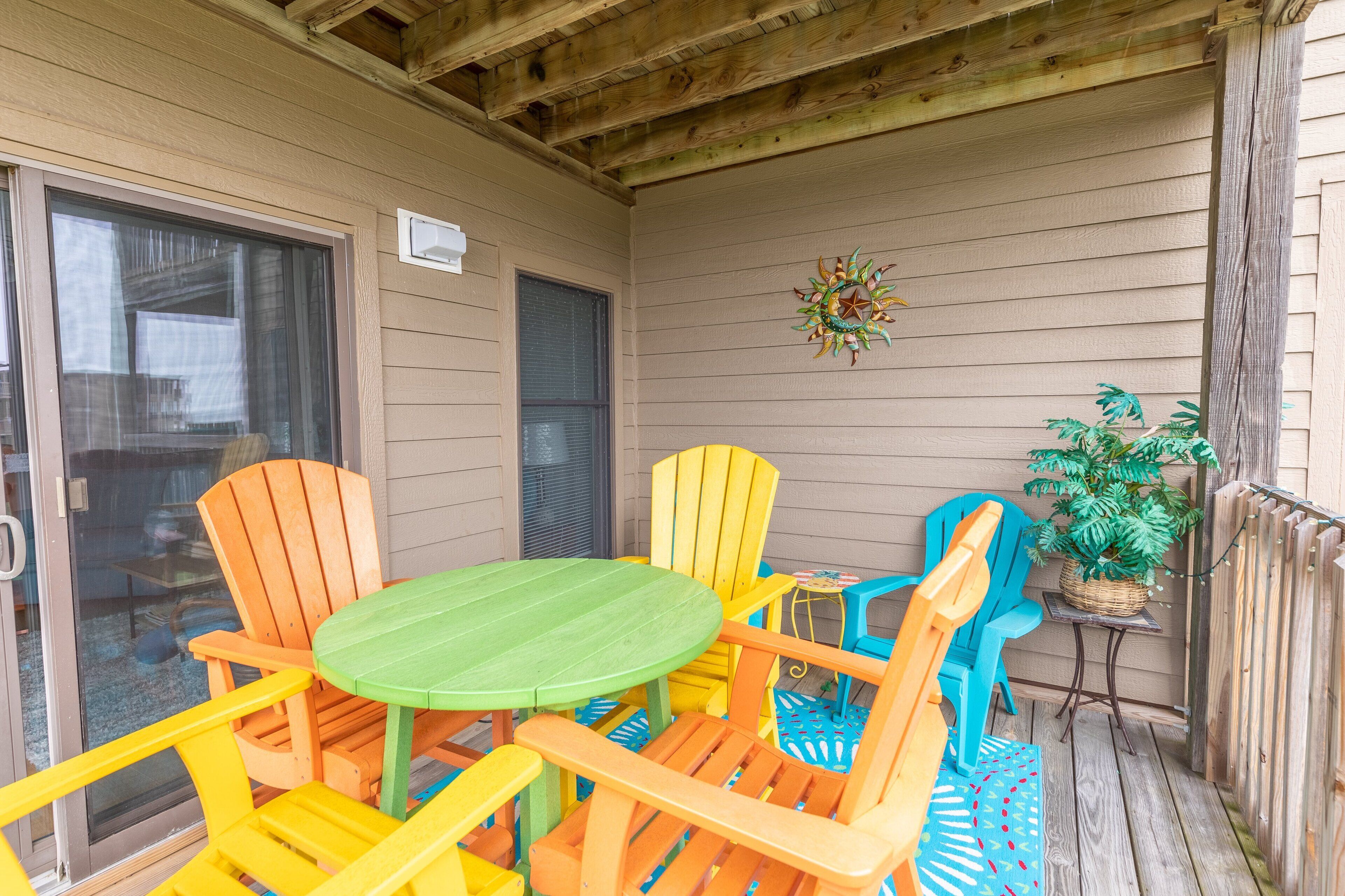 A covered patio with a wooden table and colorful Adirondack chairs.