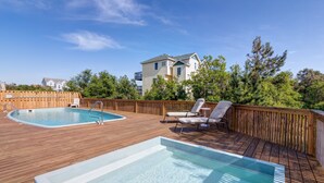 Une terrasse en bois avec deux piscines, des chaises longues et une clôture en bois.