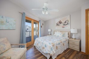 A bedroom with a bed, bedside tables, a chair, a ceiling fan, and a view through a glass door.