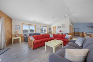 A living room with a red sectional sofa, a grey sofa, a glass coffee table, and a ceiling fan.