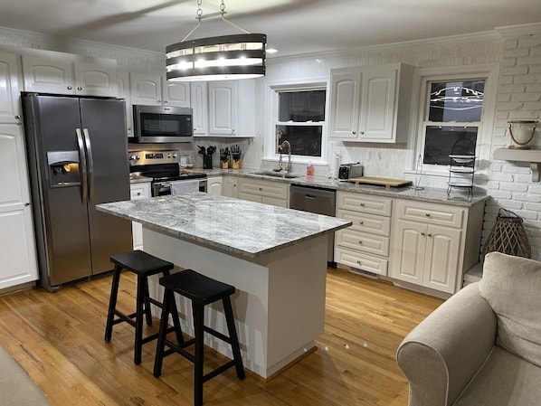 A modern kitchen with white cabinetry, a stainless steel refrigerator, a microwave, and a large island with bar stools.