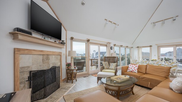 A spacious living room with a large flat-screen TV, a fireplace, a sofa, and a balcony with a view of the city. - 1067 - Easy Street - Short Walk to Beach | Pool & Hot Tub (Corolla)