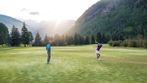 Campo de golf con montañas al fondo, que presenta un césped cuidado y árboles.