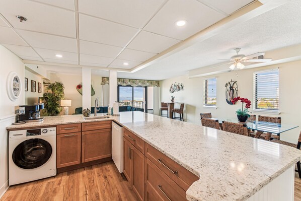 A modern kitchen with a large island, wooden cabinets, and a built-in washing machine. - XPLORIE ACTIVITIES & LINENS INCLUDED*! 3BR/2BA Capri. Spectacular Bay View! (Ocean City)