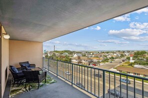 A balcony with a view of a residential area, a table with chairs, and a patterned rug. - XPLORIE ACTIVITIES & LINENS INCLUDED*! 3BR/2BA Capri. Spectacular Bay View! (Ocean City)