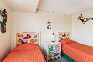 A bedroom with two beds, a nightstand, and wall decorations including a lizard and flip-flops. - XPLORIE ACTIVITIES & LINENS INCLUDED*! 3BR/2BA Capri. Spectacular Bay View! (Ocean City)