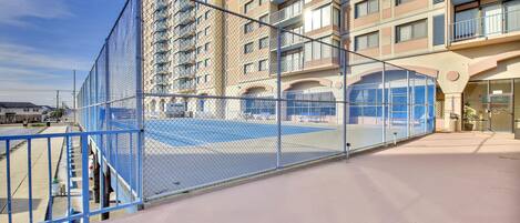 Un immeuble à plusieurs étages doté de balcons, d’un court de tennis clôturé et d’un espace de stationnement.