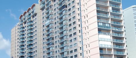 A multi-story hotel with balconies, a sandy ground floor, and a clear sky.