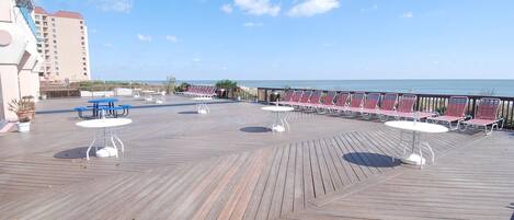 A wooden deck with tables and chairs, overlooking a body of water.
