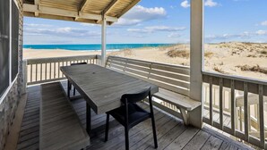 Una terrazza coperta con tavolo e sedie, con vista su una spiaggia con dune sabbiose e l'oceano.