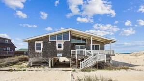 Una casa sulla spiaggia con un balcone, un portico coperto e una scalinata che conduce all'ingresso.