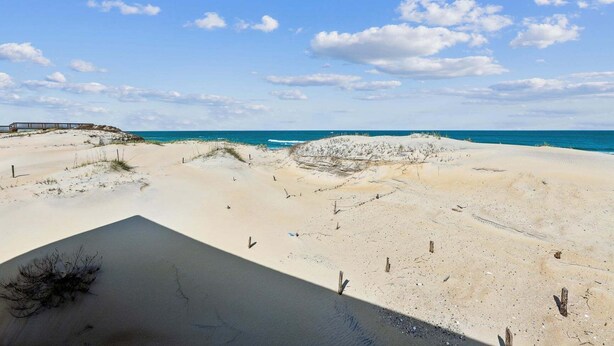 Una spiaggia con dune, una struttura in legno e un cielo sereno.