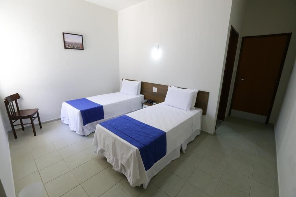 Habitación de hotel con dos camas individuales, una silla de madera, una mesita y una puerta.