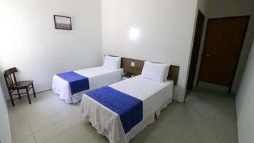 Habitación de hotel con dos camas individuales, una silla de madera, una mesita y una puerta.