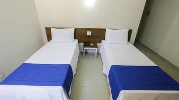 Quarto de hotel com duas camas de solteiro, cada uma com colcha branca e azul, cabeceira de madeira e uma pequena mesa de cabeceira com telefone.