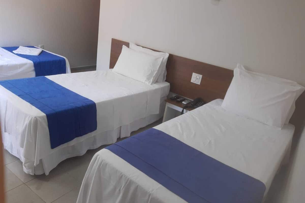 A hotel room with two beds, each with a white and blue bedspread. There is a wooden headboard on one bed and a small bedside table with a phone.