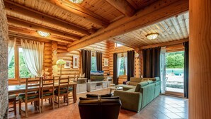Interior acolhedor de uma cabana de madeira, com espaço de jantar, sofá e televisão.