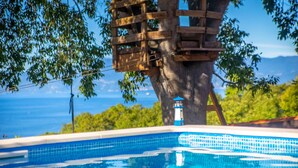 A swimming pool with a wooden structure attached to a tree, a lighthouse, and a view of the sea. - Beach front home in Kostrena (Kostrena)