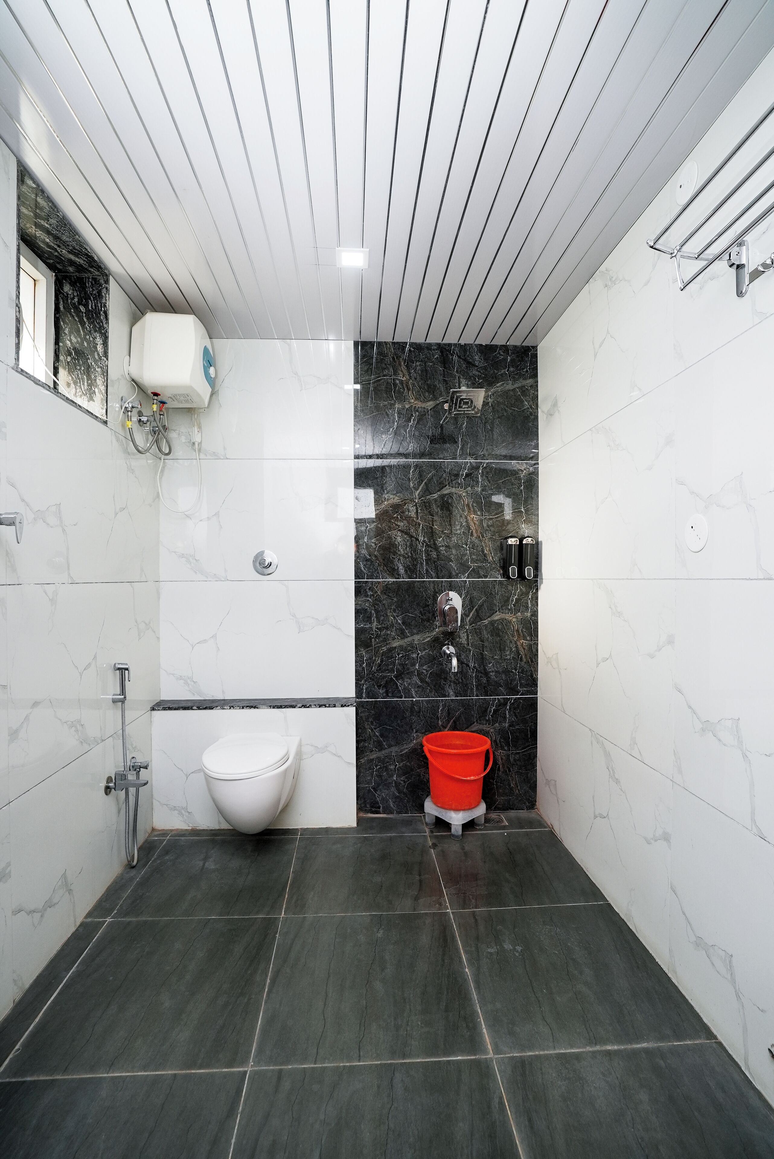 A modern bathroom with a white toilet, a shower area, and a red bucket.