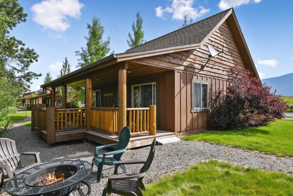 A wooden cabin with a porch, a fire pit, and outdoor seating.