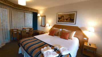 Quarto de hotel com uma cama grande, duas mesas de cabeceira, uma escrivaninha com cadeira e uma janela com cortinas.
