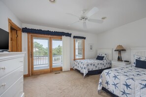 Une chambre dotée d’un ventilateur de plafond, de deux lits avec une literie à motifs d’étoiles, d’une table de chevet avec une lampe et d’une vue sur l’extérieur grâce à une porte-fenêtre coulissante.