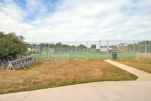A tennis court with a fence, a sign, and bicycles parked nearby.