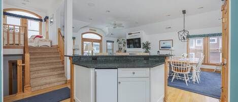 A modern kitchen with a central island, white cabinetry, and a dining area with a wooden table and chairs.