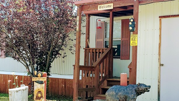 Un bâtiment en bois avec une pancarte « Bienvenue », un panneau d’avertissement et une statue d’ours à l’extérieur.
