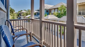 A covered outdoor area with a railing, two wicker chairs, and a view of neighboring houses.