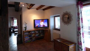 Ein Wohnzimmer mit Fernseher, Bücherregalen, einem Holzschrank und einem Fenster mit Vorhängen.