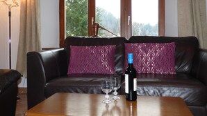 Ein Wohnzimmer mit einer Ledersofa, zwei gemusterten Kissen, einem Holztisch und einer Weinflasche.