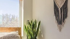 Quarto com cama, planta em vaso, tapeçaria de macramé e ar condicionado.