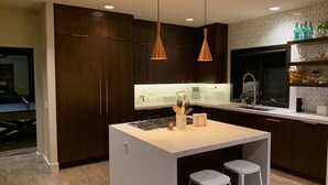 A modern kitchen with dark wood cabinets, a white island with stools, pendant lighting, and a tiled backsplash. - Beautiful and Spacious home only 5 minute drive to Canyons Resort---Sleeps 10 (Park City)