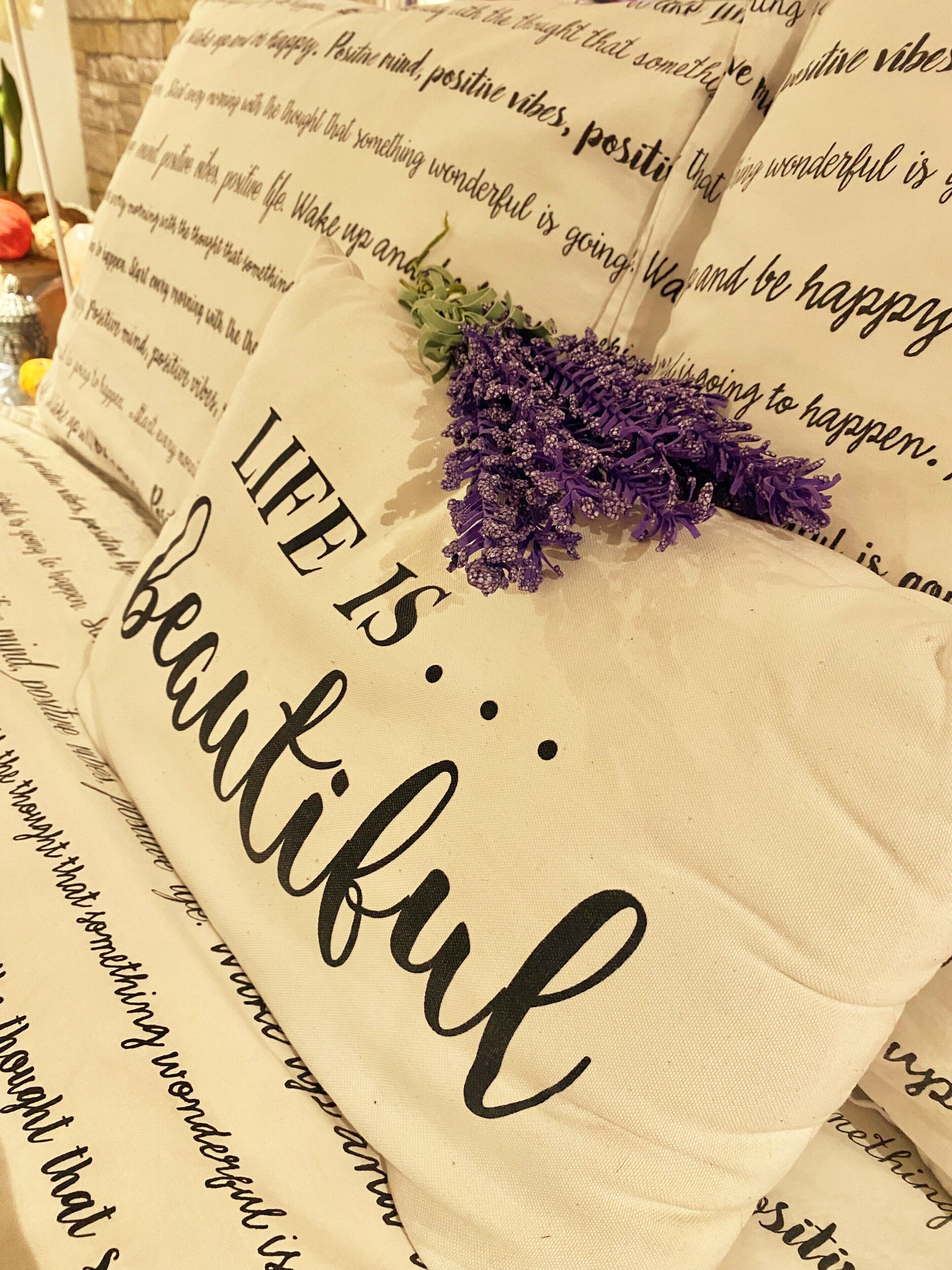 Un almohadón con el texto 'LIFE IS... beautiful' y flores moradas.
