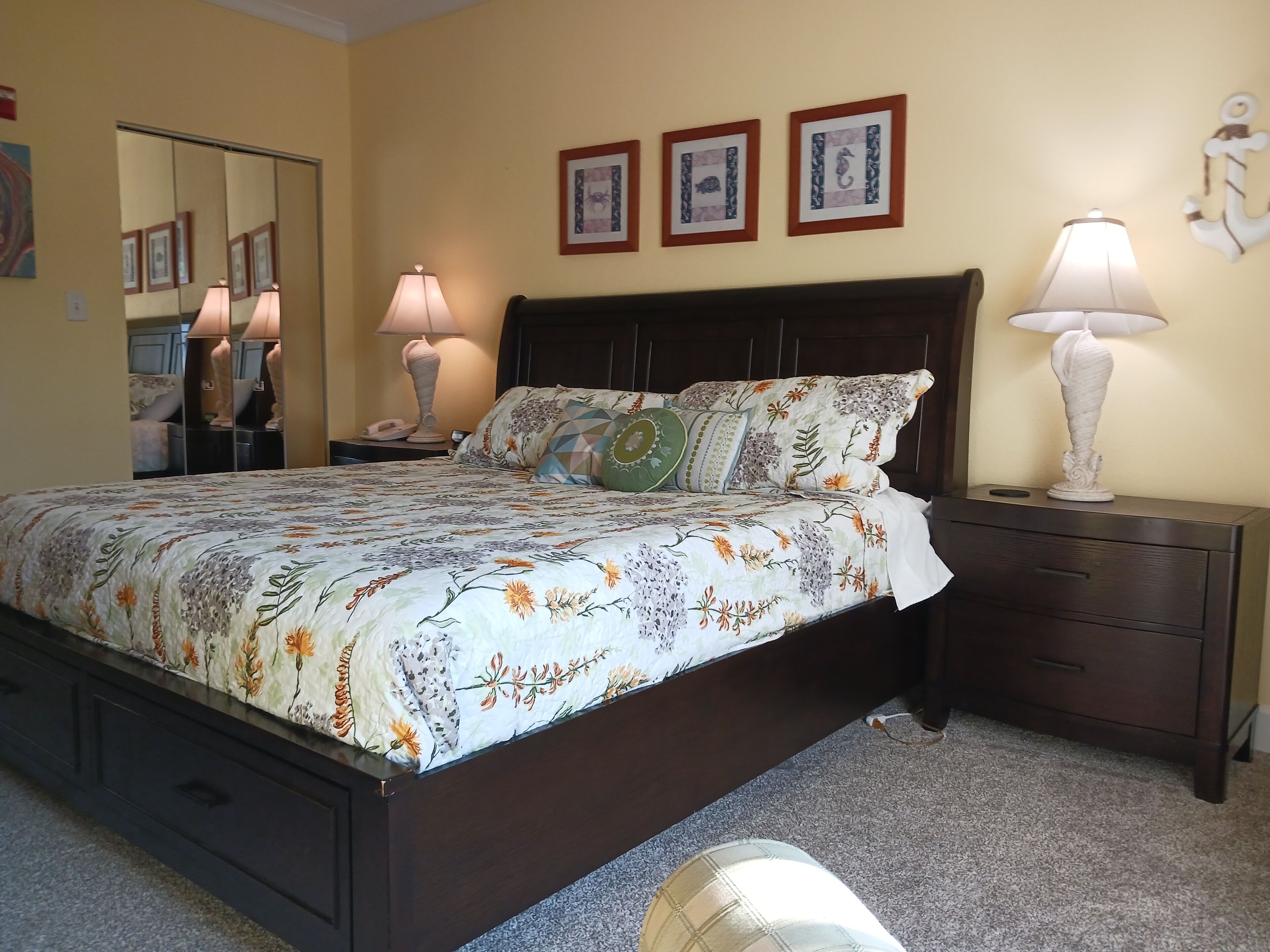 Quarto com uma cama grande, duas mesas de cabeceira, um criado-mudo, um espelho e três quadros na parede.