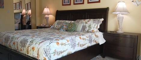 Quarto com uma cama grande, duas mesas de cabeceira, um criado-mudo, um espelho e três quadros na parede.